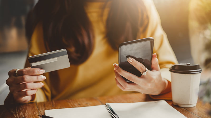 Mujer realizando una transacción con una tarjeta y su notebook